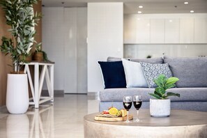 A modern living room with a grey sofa, a round coffee table with snacks and drinks, and a potted plant. - Surf & Sunrise Beachfront Hideaway by Inn Paradise (Surfers Paradise)