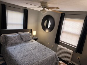 Ein Schlafzimmer mit Bett, Deckenventilator, rundem Spiegel, Nachttischlampe und Heizkörper.