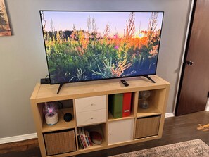 Television on puisen jalustan päällä, mukana kaukosäädin. Televisiota ympäröivät säilytyslaatikot ja -laatikostot.
