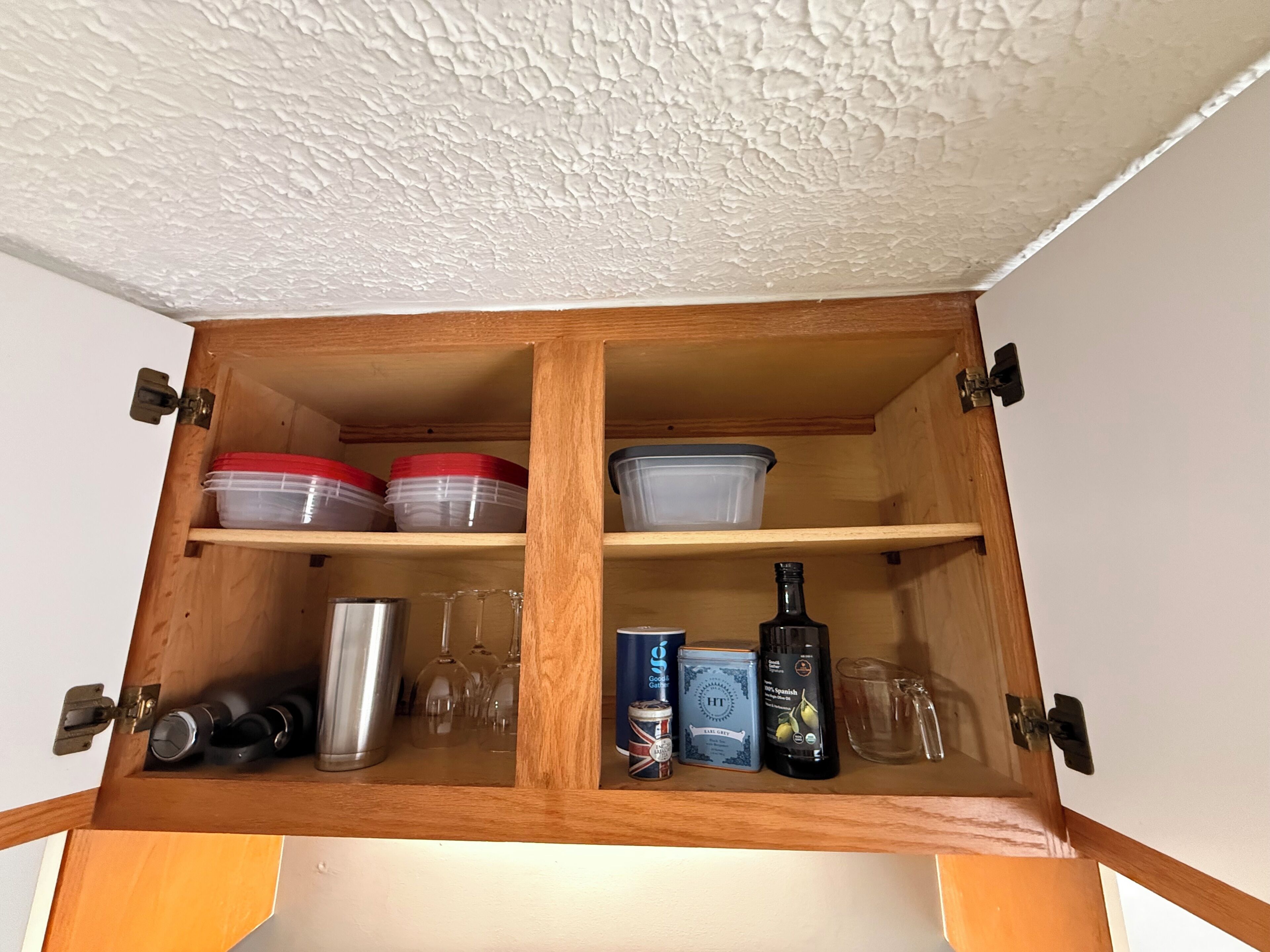 Un meuble en bois doté de deux étagères, contenant des ustensiles de cuisine, une bouteille et une boîte en métal.