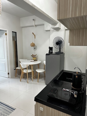 A modern kitchen with a black countertop, a coffee maker, a fan, and a dining area with a white table and chairs.