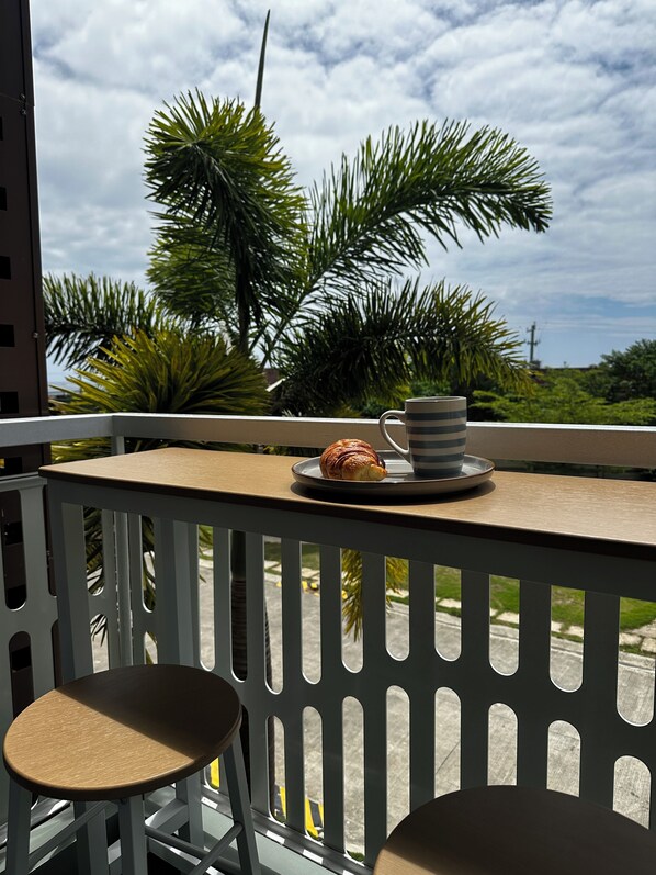 Un balcon avec une table, une chaise, une assiette contenant un croissant et une tasse.