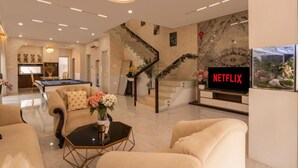 Un salon moderne doté d’une table de billard, de sièges confortables, d’un escalier agrémenté de décorations festives et d’un téléviseur affichant le logo « NETFLIX ».
