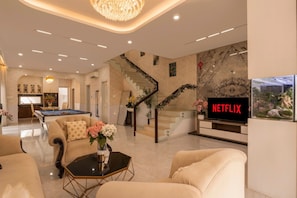 A modern living room with a pool table, comfortable seating, a staircase with festive decorations, and a TV displaying 'NETFLIX'. - D2 Center Pool Villa with 6 bedrooms (An Khanh Ward)