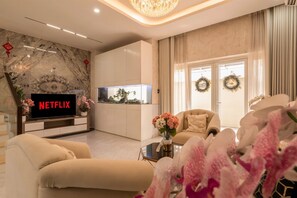 Uma sala de estar moderna com televisão de tela plana, assentos confortáveis, uma mesa de centro de vidro e guirlandas decorativas nas janelas.