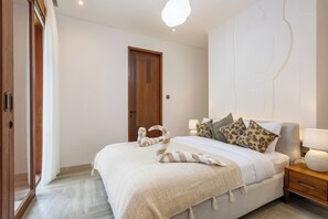 Een slaapkamer met een bed, kussens, een nachtkastje, een houten deur en een lamp.