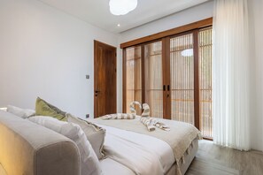 A bedroom with a bed, a sofa, a wooden wardrobe, and a sliding door with vertical blinds. - Villa Albizia - 2BR private pool villa near Canggu (Mengwi)
