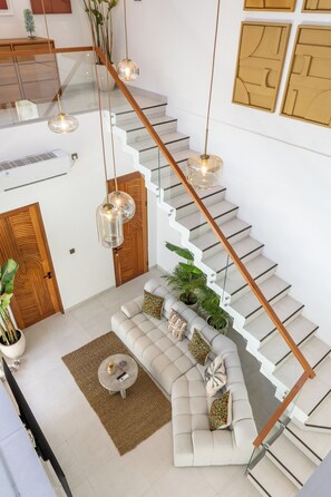 Een modern interieur met een trap, een zithoek met een bank en salontafel, en hangende pendantlampen.
