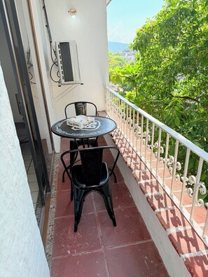 Varanda com mesa e cadeiras, um ar condicionado e vista para o verde.
