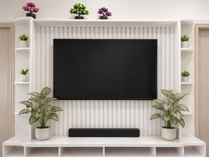 Una sala de estar moderna con un televisor de pantalla plana grande montado en una pared blanca, flanqueado por estanterías blancas con plantas en macetas.