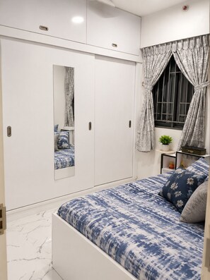 Un dormitorio con cama, armario, ventana con cortinas y una planta pequeña.