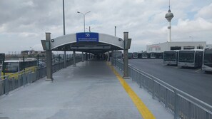 Ein Busbahnhof mit überdachtem Gang, Busse auf der rechten Seite und ein Turm im Hintergrund.