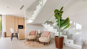 Un intérieur moderne avec un escalier, deux fauteuils, une plante en pot et un coin cuisine.