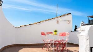 Eine Dachterrasse mit weißer Wand, einem Tisch mit Stühlen und einem kleinen Topfpflanzen.