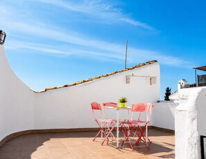Eine Dachterrasse mit weißer Wand, einem Tisch mit Stühlen und einem kleinen Topfpflanzen.