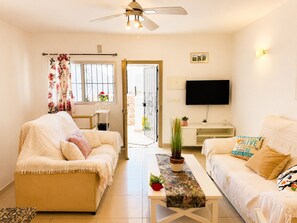 Ein Wohnzimmer mit zwei Sofas, einem Couchtisch, einem Fernseher und einer Tür, die nach draußen führt.