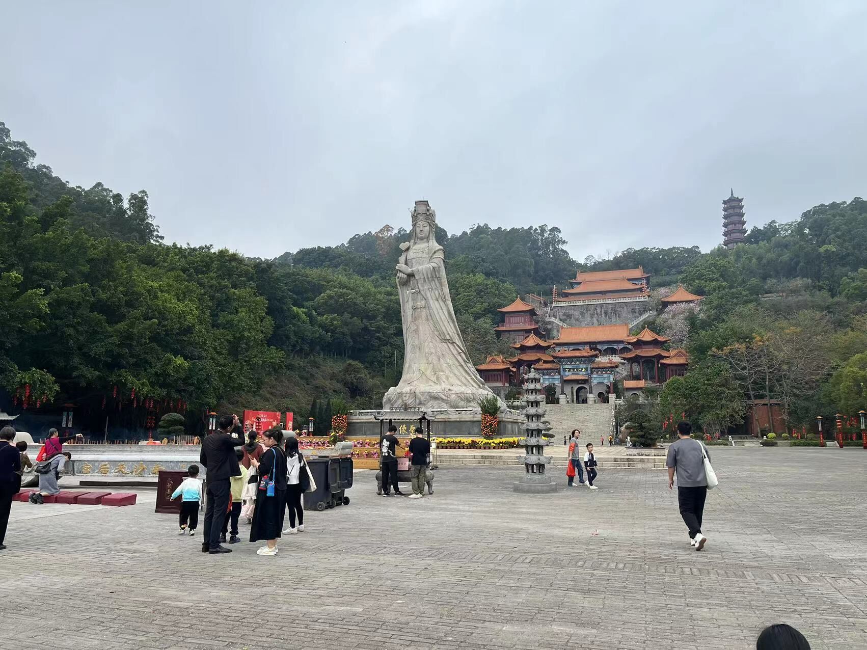 A large stone statue in a public square with traditional architecture in the background.