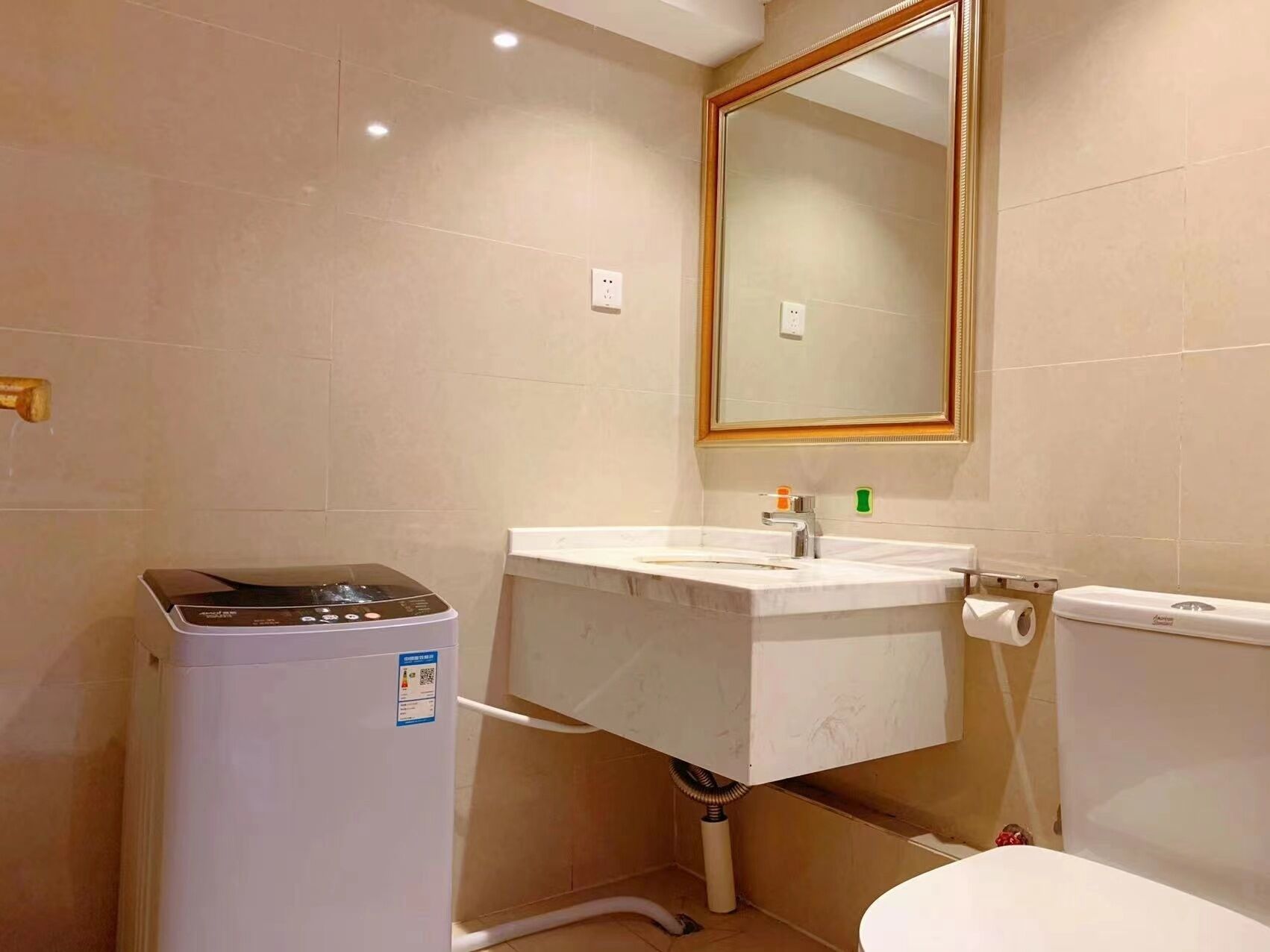 A bathroom with a washing machine, a sink, a toilet, and a mirror.