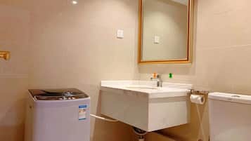 A bathroom with a washing machine, a sink, a toilet, and a mirror.