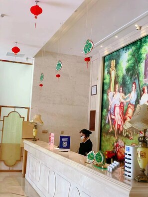 A reception desk with a large painting, red hanging decorations, and a framed certificate on the wall. - Vienna International Hotel (GUANGZHOU)