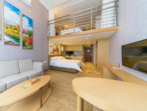 A hotel room with a loft bed, a sofa, a dining table, a TV, and artwork on the walls.