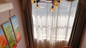 Una habitación con una mesa de comedor, sillas, un candelabro y un amplio ventanal con cortinas translúcidas.
