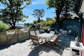 A wooden deck with a table and chairs, surrounded by greenery and a view of the sea. - 4 star holiday home in KARLSHAMN (KARLSHAMN)