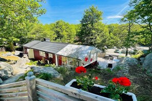 A rustic cabin with a metal roof, surrounded by greenery and rocks. - 4 star holiday home in KARLSHAMN (KARLSHAMN)