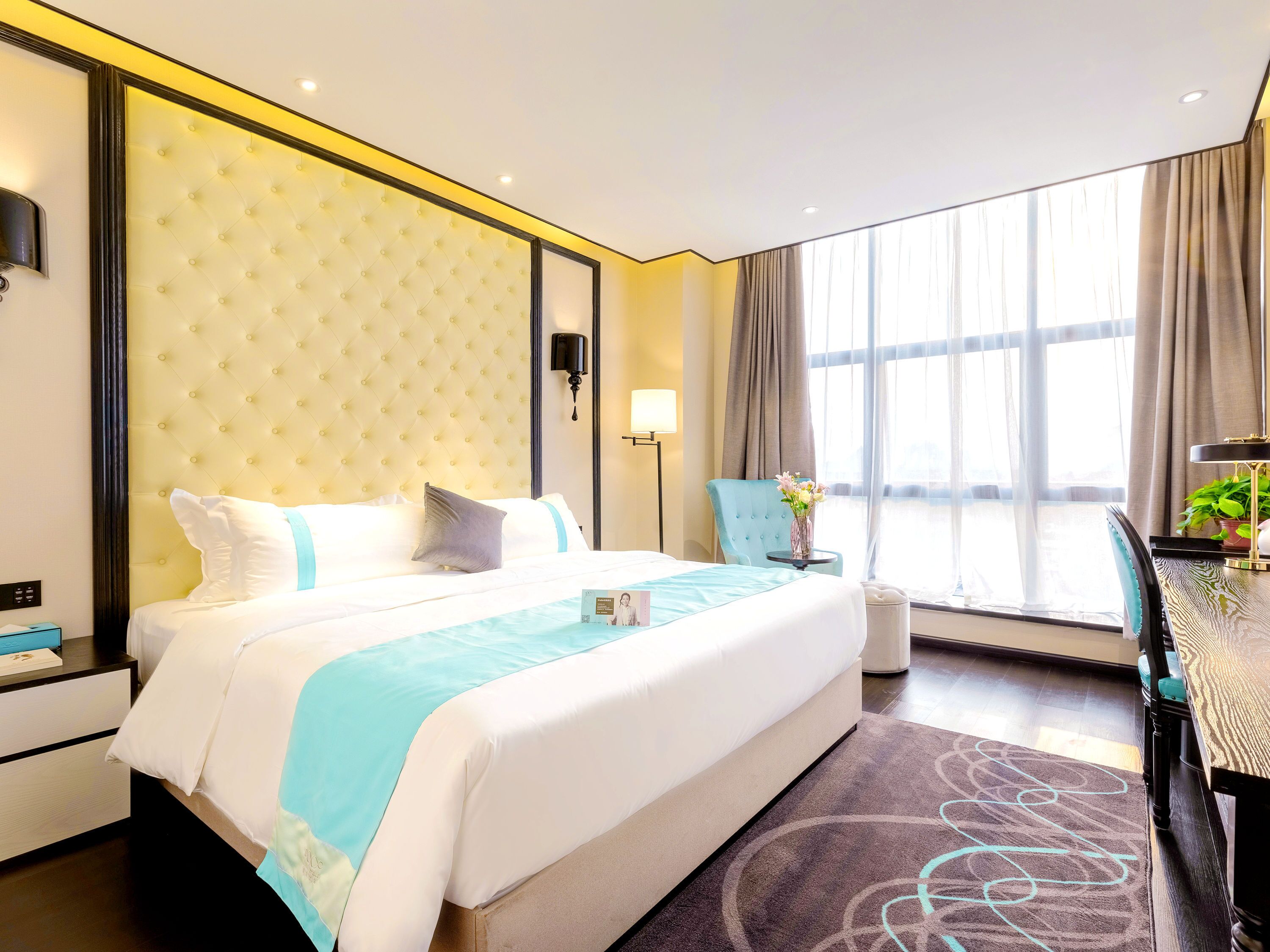 A hotel room with a large bed, bedside tables, a desk, a chair, a lamp, and a window with curtains.