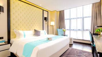 A hotel room with a large bed, bedside tables, a desk, a chair, a lamp, and a window with curtains.