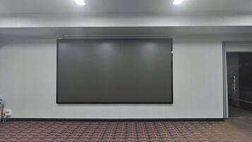 Un salón de conferencias con una pantalla de proyección grande, una puerta y un suelo de baldosas.
