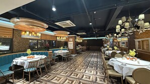 Ein Restaurant mit mehreren Tischen und Sitzecken, Deckenventilatoren und Pendelleuchten.