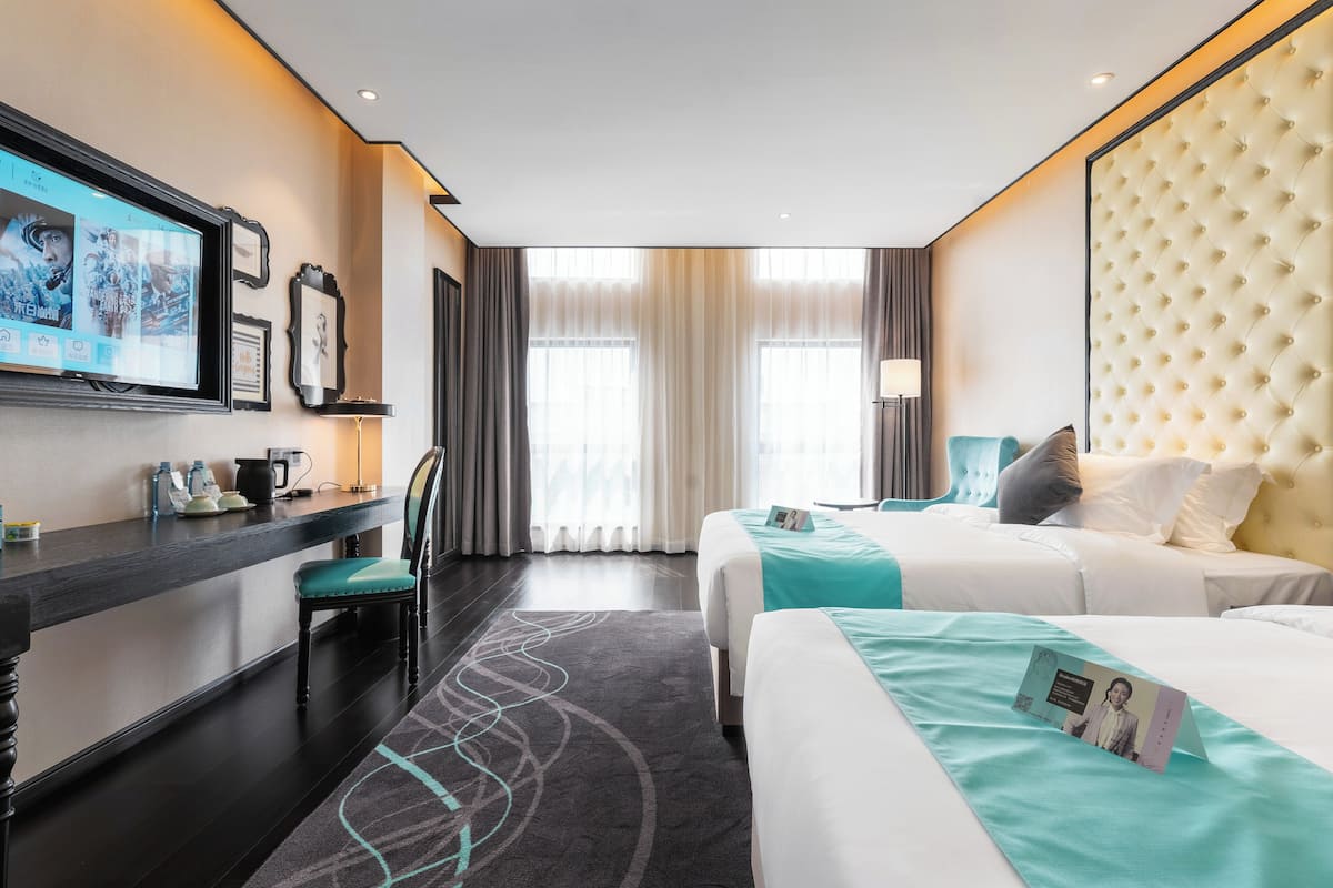 Una habitación de hotel con cama, escritorio, silla, televisor y ventana con cortinas.