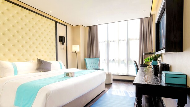 Ein Hotelzimmer mit einem großen Bett, einem Schreibtisch, einem Stuhl, einem Fernseher und einem Vorhangfenster.