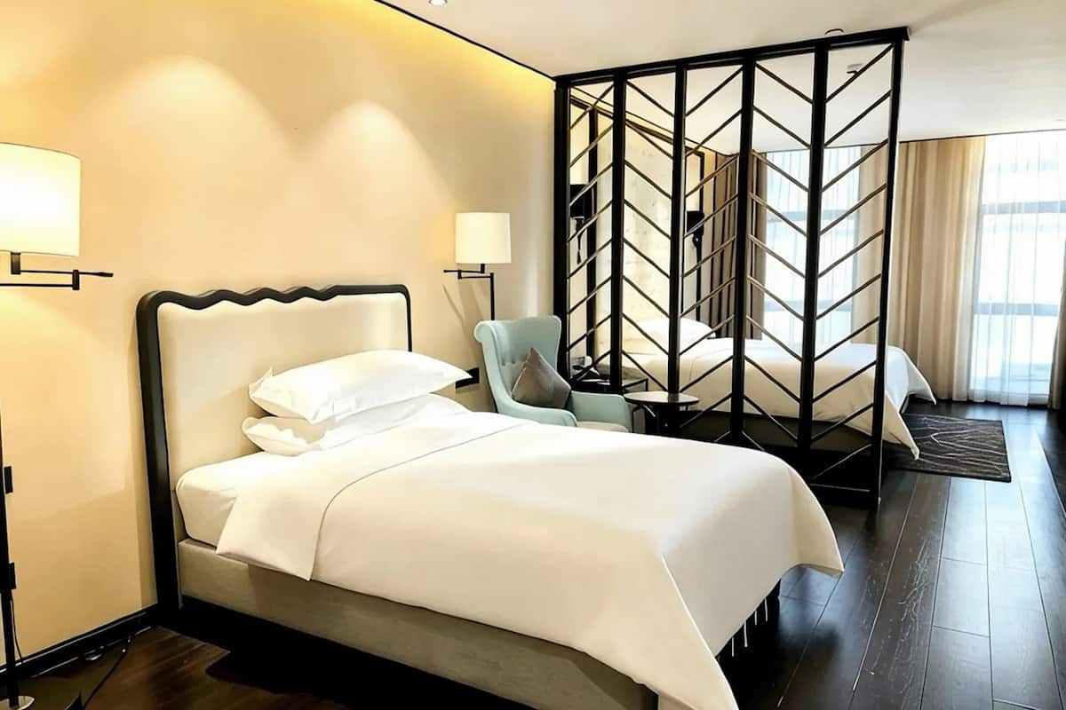 Una habitación de hotel con una cama, una silla, un escritorio, una lámpara y un separador con diseño geométrico.