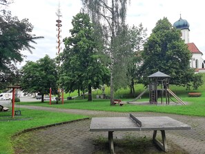 Een park met een speeltuin, een kiosk en een kerk op de achtergrond.