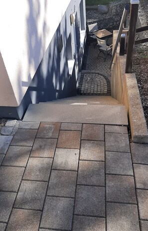 Un espacio exterior pavimentado con un sendero de ladrillo que lleva a una terraza de madera.