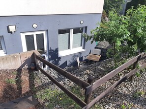 Ein Wohngebäude mit Balkon, Holzzaun und Gartenanlage mit Pflanzen und einem kleinen Tisch.