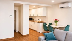 A modern kitchen with white cabinets, a wooden countertop, and a dining area with green chairs and a table.