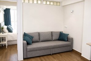 Una habitación en tonos neutros con un sofá gris, una mesita blanca y un ventanal con cortinas.