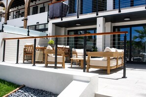 Un área de estar al aire libre de estilo moderno con mobiliario de madera y barandilla de vidrio.