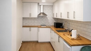 A modern kitchen with white cabinets, a wooden countertop, a stainless steel range hood, and a built-in sink.