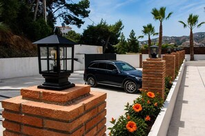 Un SUV negro estacionado en un camino de entrada pavimentado, con una estructura de ladrillo y un jardín lleno de flores naranjas.