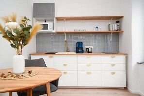 Uma cozinha moderna com armários brancos, bancada de madeira, micro-ondas, cafeteira e um vaso com plantas secas na mesa.