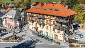 A traditional half-timbered building with a red-tiled roof, multiple balconies, and a street view with parked cars and a pedestrian crossing. - Faraway Homes Studio Semmering #303 (Spital am Semmering)