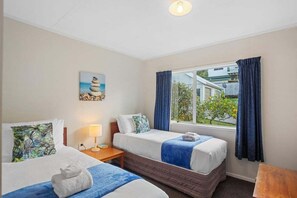 Ein Hotelzimmer mit zwei Betten, einem Fenster mit Vorhängen, einem Gemälde an der Wand und einer Lampe auf dem Nachttisch.