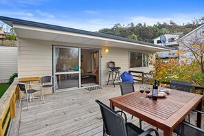 Eine Holzterrasse mit Tisch, Stühlen, einer Schiebetür und einem Grill.