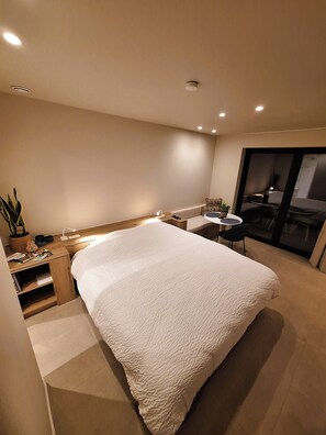 Un dormitorio moderno con una cama grande, una mesita de noche y una pequeña zona de escritorio.