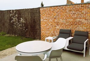 Un patio con una mesa redonda y dos sillas, un muro de ladrillo y un área con césped.