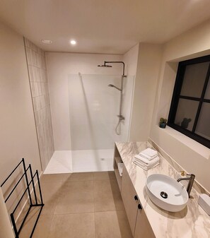 Een moderne badkamer met een glazen douchecabine, een marmeren aanrecht en een wastafel.